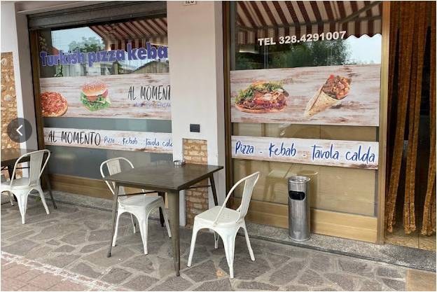 Ingresso con insegna e tavolini esterni del locale di pizza e kebab a Rovato